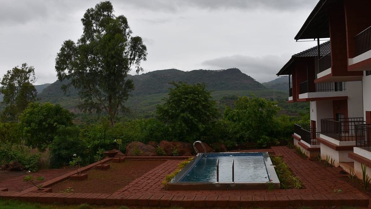 A resort with a swimming pool and a building with burgundy accents, set against a mountainous landscape under a cloudy sky.