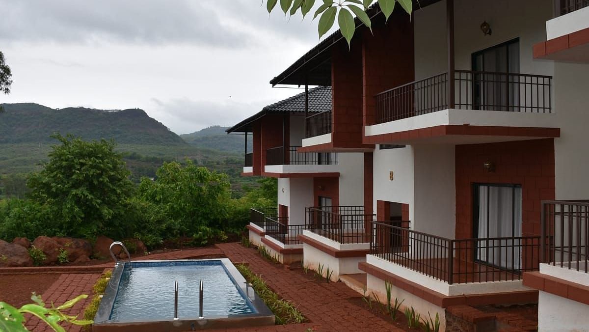 A resort with white and burgundy buildings, a swimming pool, and a mountain view under a cloudy sky.