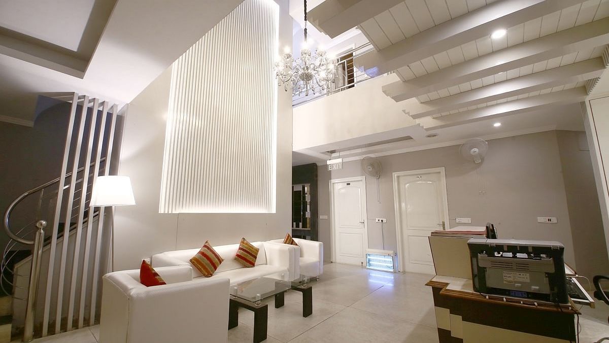 A hotel lobby with a white sofa, decorative pillows, a textured wall with lighting, a spiral staircase, and a reception desk, lit by a chandelier. - Hotel Diamond Plaza, Chandigarh.