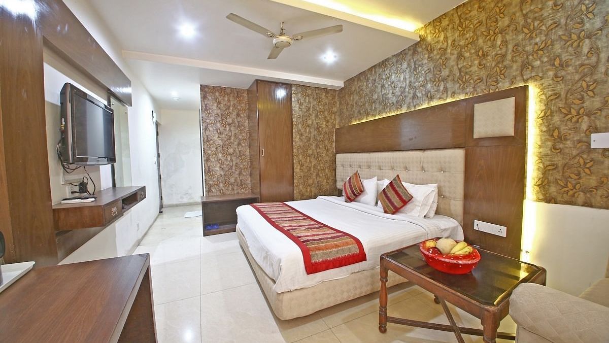A hotel room with a textured accent wall, a plush bed with decorative pillows, a wooden table, and a TV, illuminated by warm ceiling lights. - Hotel Diamond Plaza, Chandigarh.