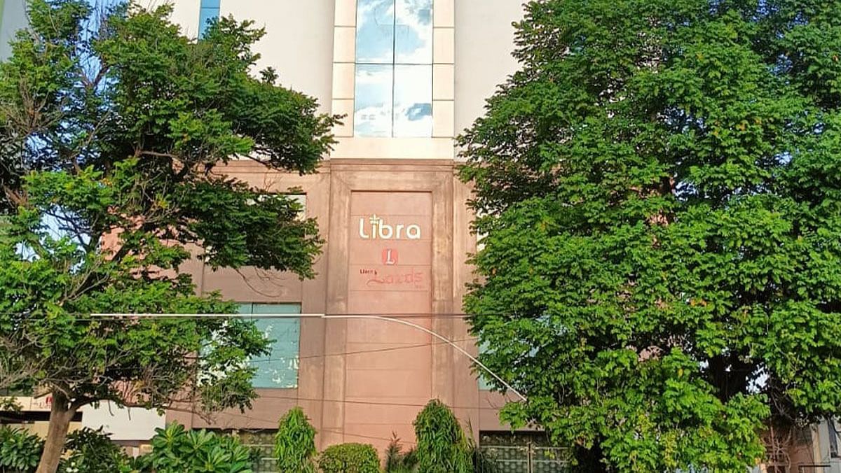 A building with a sign is partially obscured by lush green trees and landscaping.