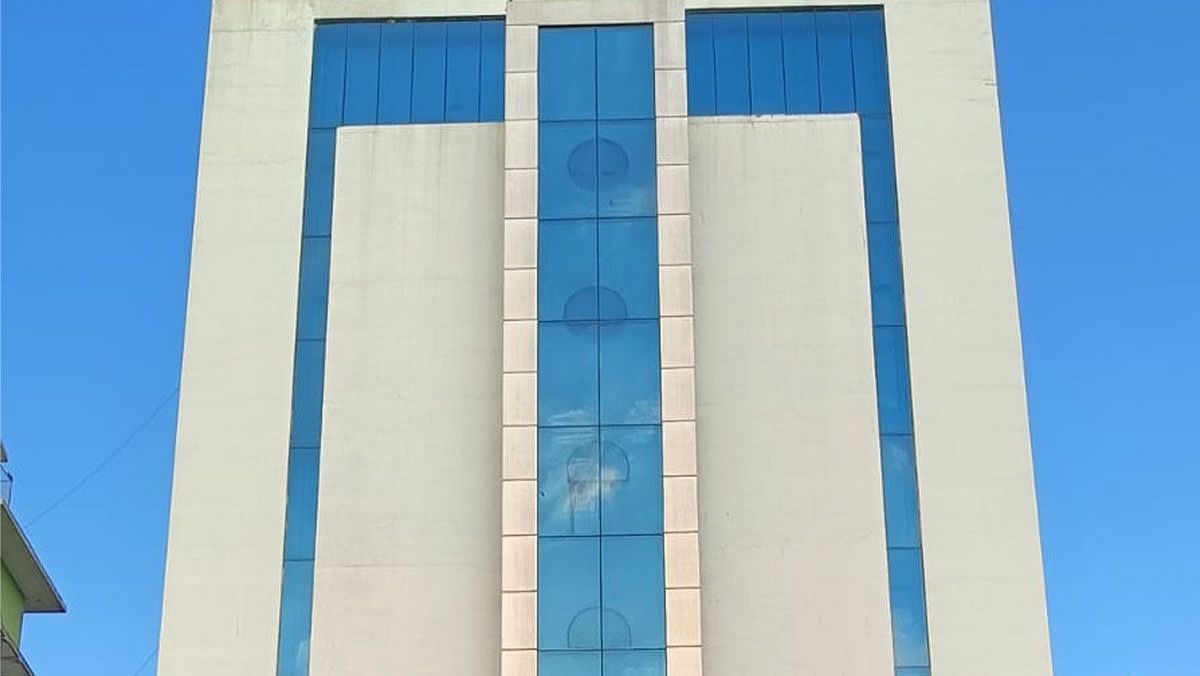 A tall building with reflective windows stands against a clear sky. The top of the building features signage.