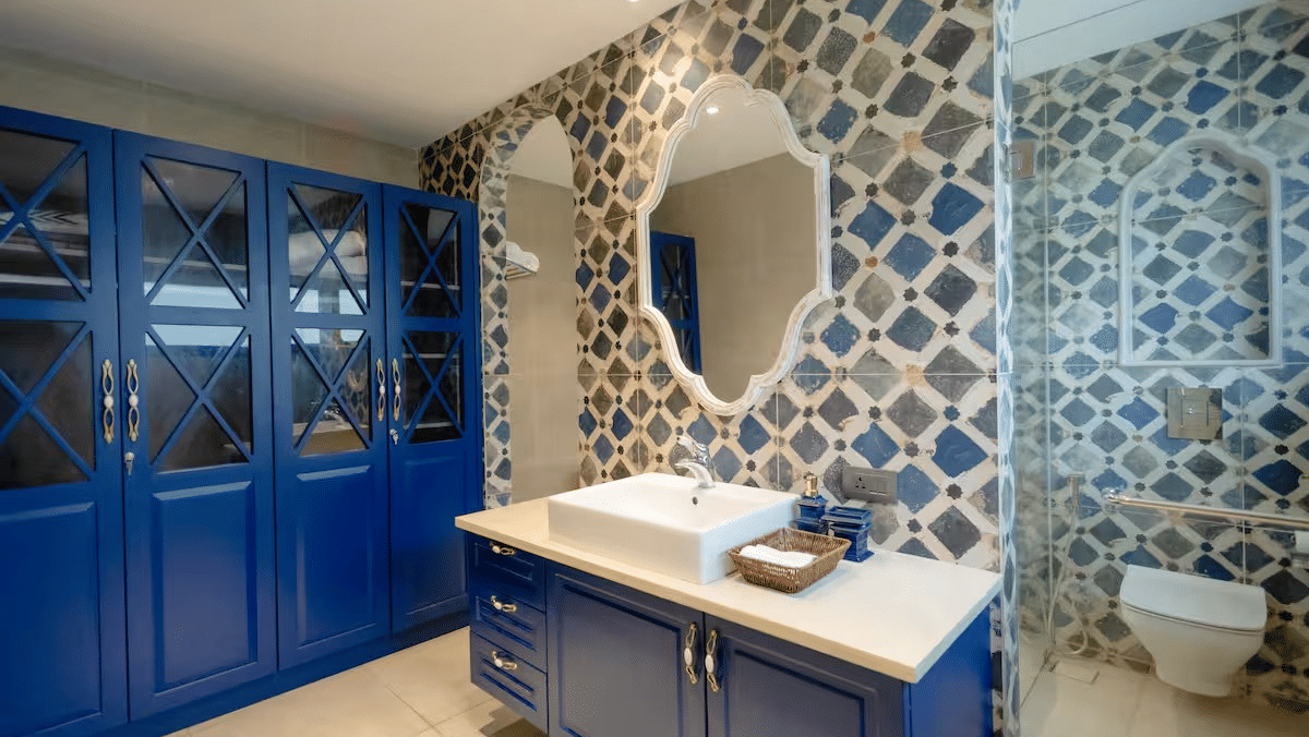 Bathroom of Lime Tree Hotels & Service Apartment Private Limited featuring blue cabinetry, patterned wallpaper, and a mirror positioned above the sink.