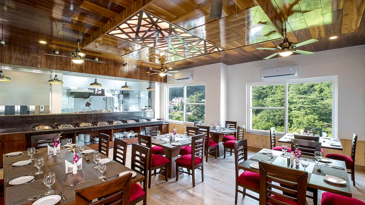Full view shot of the restaurant at Regenta Inn DLS with neatly arranged dining tables with ample of natural lighting inside.