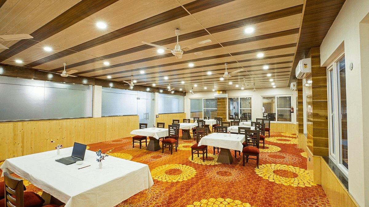 A warmly lit Banquet Hall with a fully carpeted floor along with tables set with white table cloth at Regenta Inn DLS.