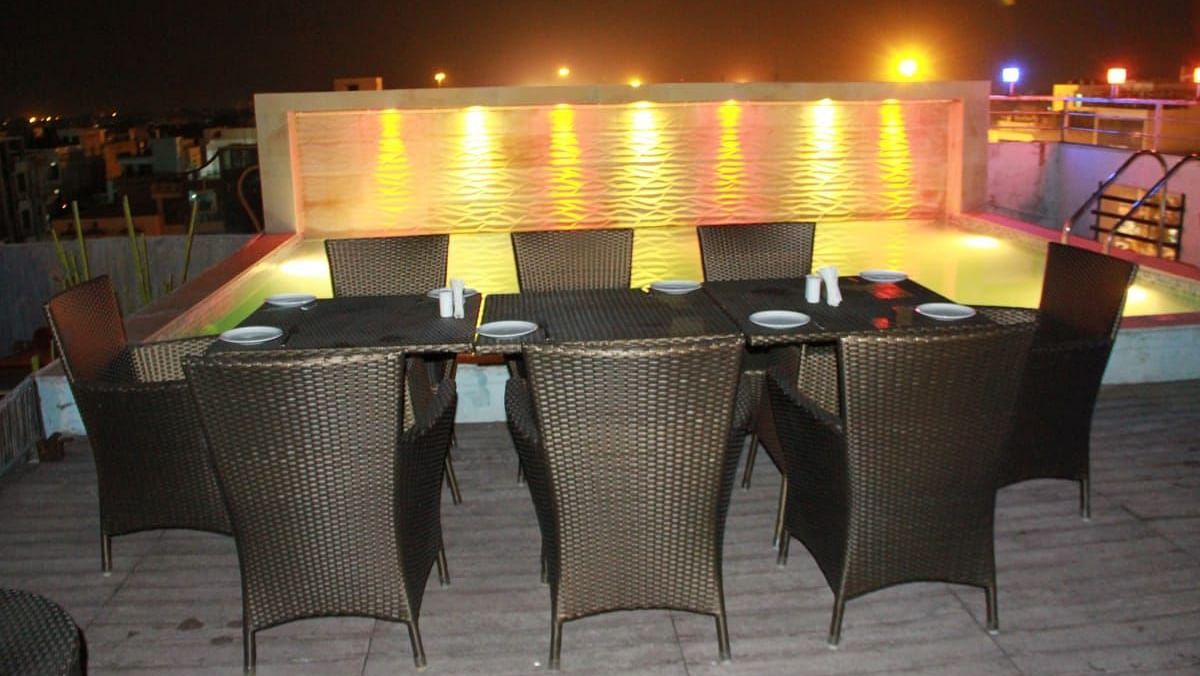 A night time view of a rooftop restaurant with illuminated wicker tables and a lit pool in the background - TGI Apple Inn, Jaipur 