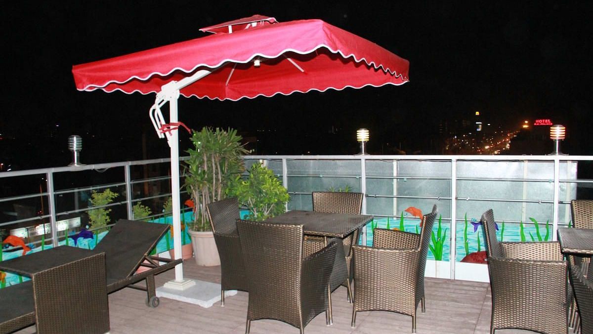A roof top dining area at night with a red umbrella, wicker chairs and city lights in the background - TGI Apple Inn, Jaipur 