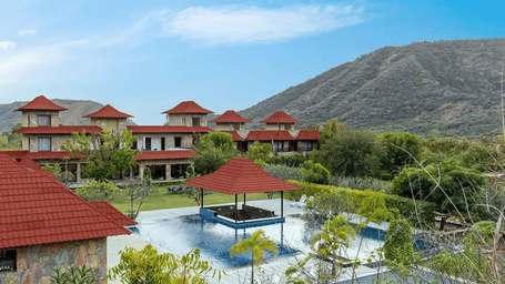 A panoramic shot of the swimming pool area surrounded by the lush greenery along with the Aravalli hills in the background.