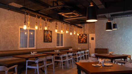 An indoor restaurant dining area with warm hanging Edison bulb lighting and wooden tables at The Bull Boutique Hotel.