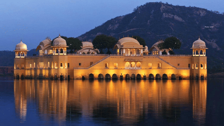 An illuminated palace-like building at night, reflected in the water.