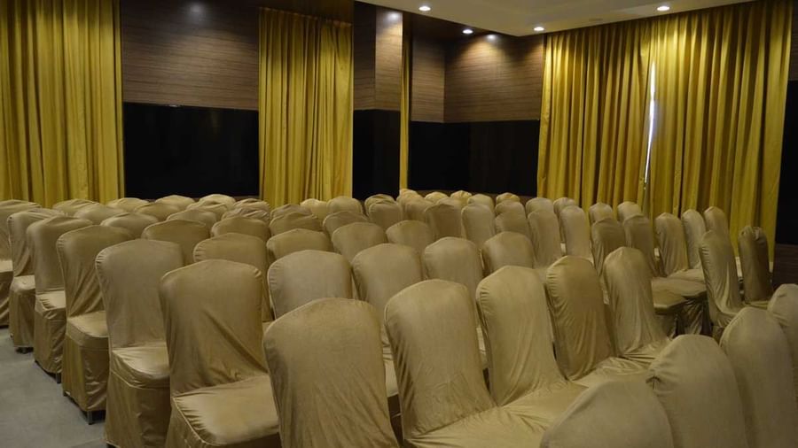 A wide-angle view of a banquet hall at The Royal Comfort, showing multiple rows of chairs ready for an event, with yellow and black curtains in the background.