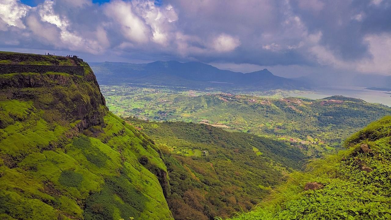 an image of a cliff next to green terrain and a cloudy sky