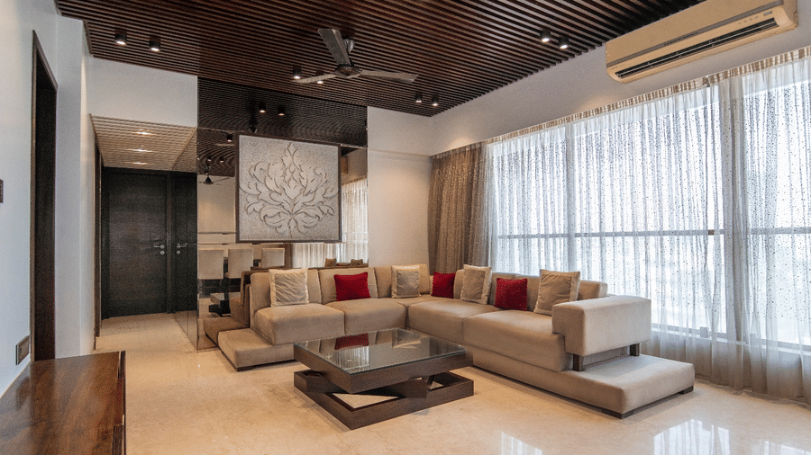 Living room at Theory9 - Premium Serviced Apts, Khar, featuring a tan sectional sofa, red accent pillows, and dark wood slatted ceiling.