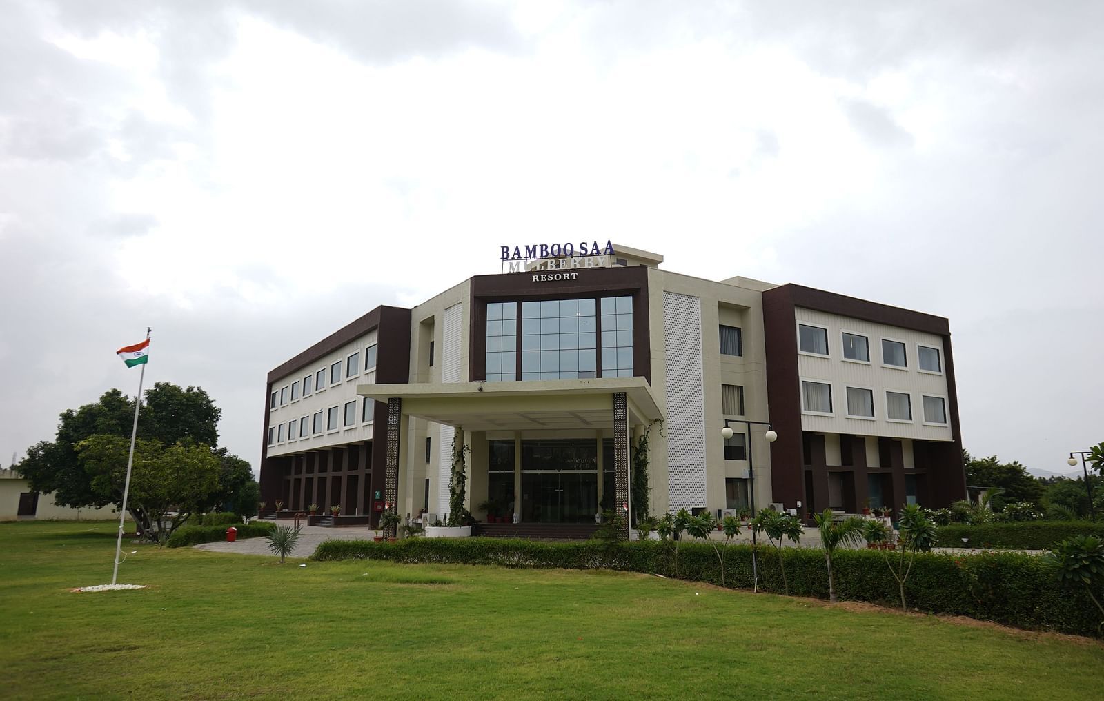 Exterior view of Bamboo Saa Mulberry Resort, Pushkar, Rajasthan featuring a modern building with a light-coloured facade with a lawn in the foreground