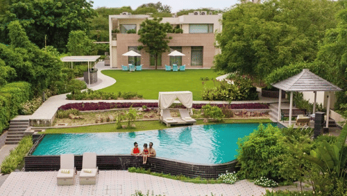 An far out view of a villa with a family sitting on the side of the swimming pool - Karma Lakelands.