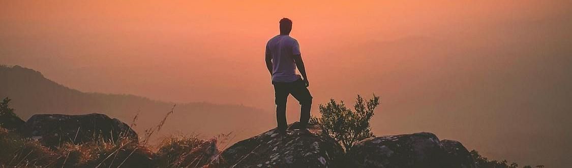 Image of a person standing on a cliff with the sun in front.