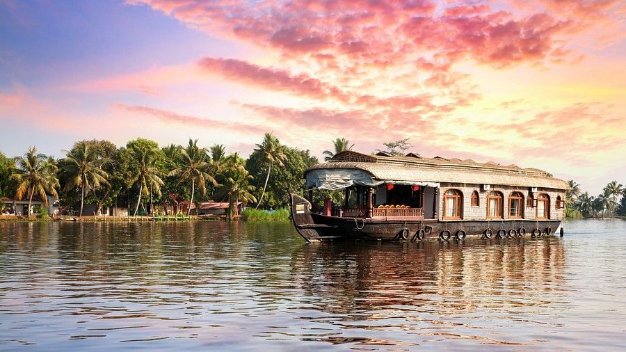 A boathouse floating in a small river surrounded by palm trees. At the horizon there is a sky in turned into evening hues.