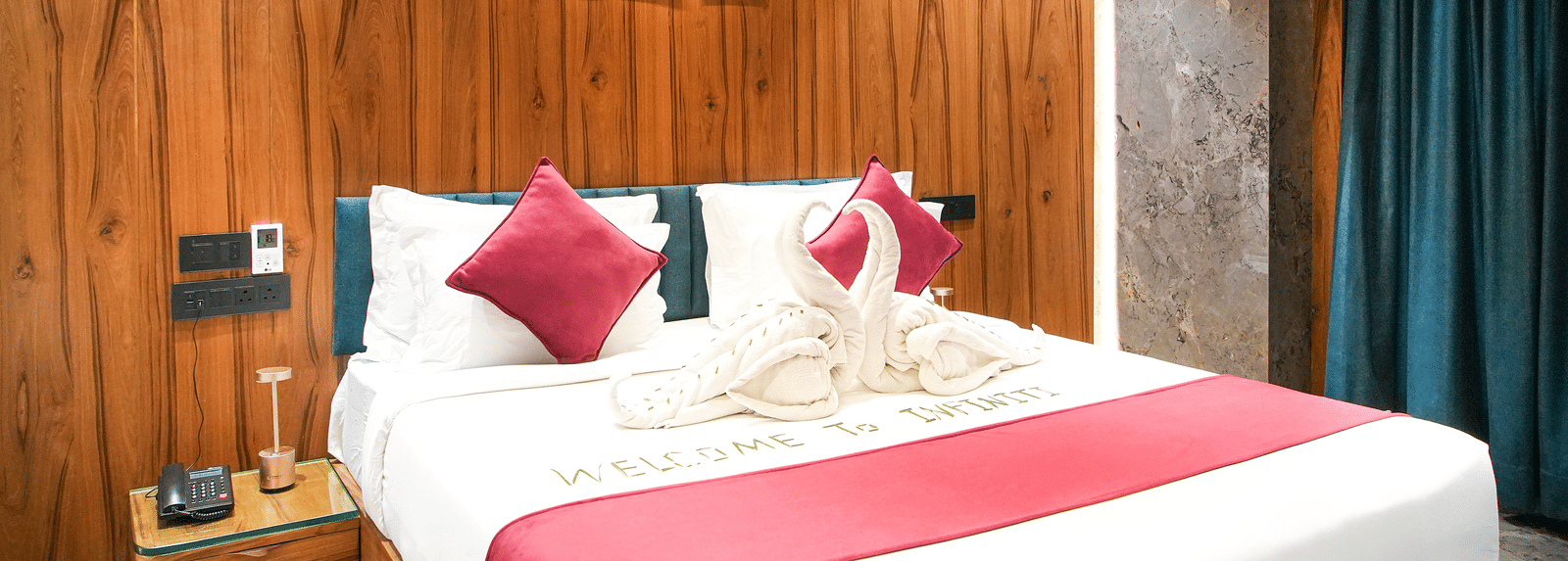Wooden-panelled bedroom with king bed, red cushions, and dark curtains at Infiniti Hotel, Indore.