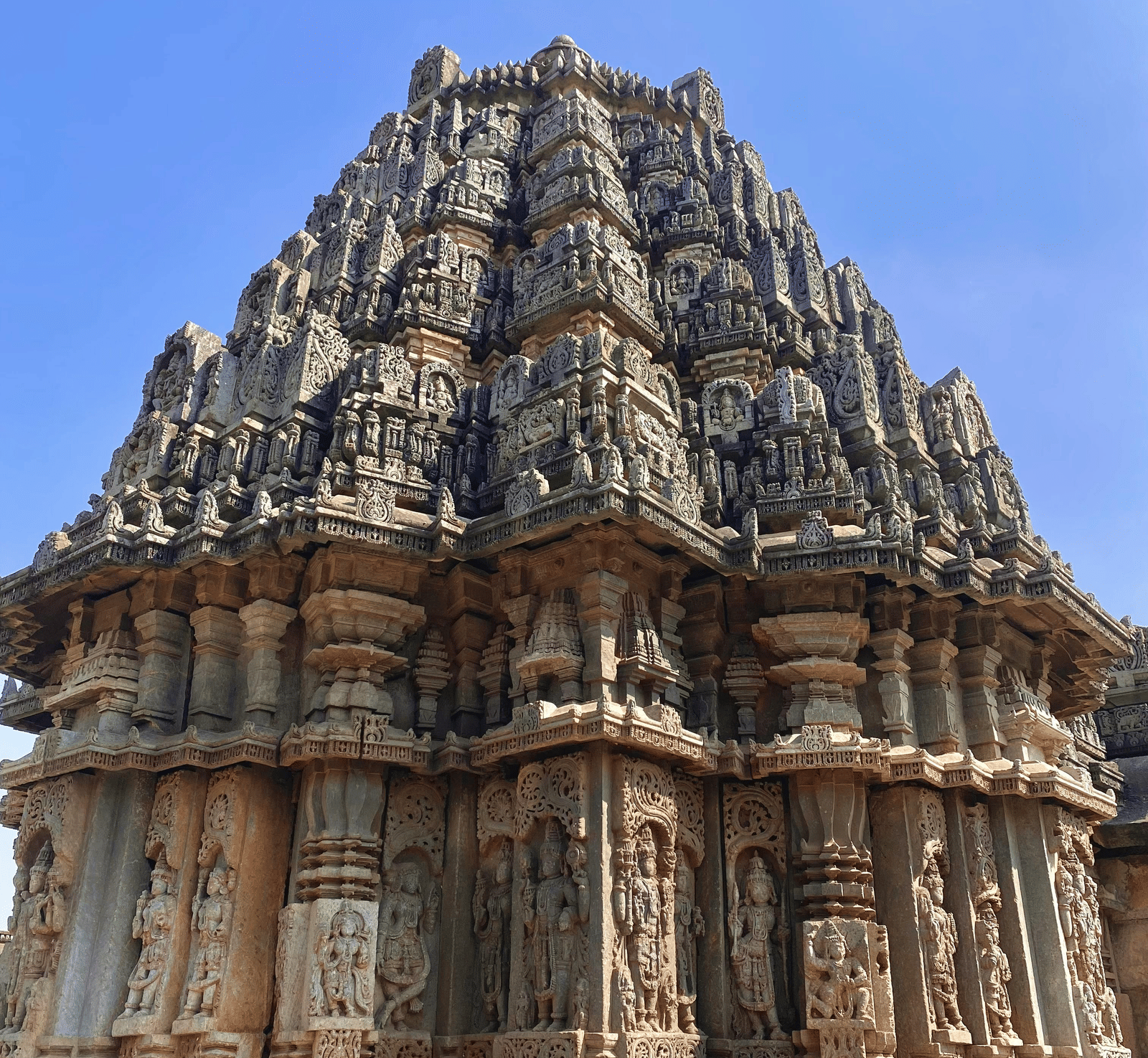 A close-up of an ornate historic Indian temple spire with intricate stone carvings under a clear blue sky.