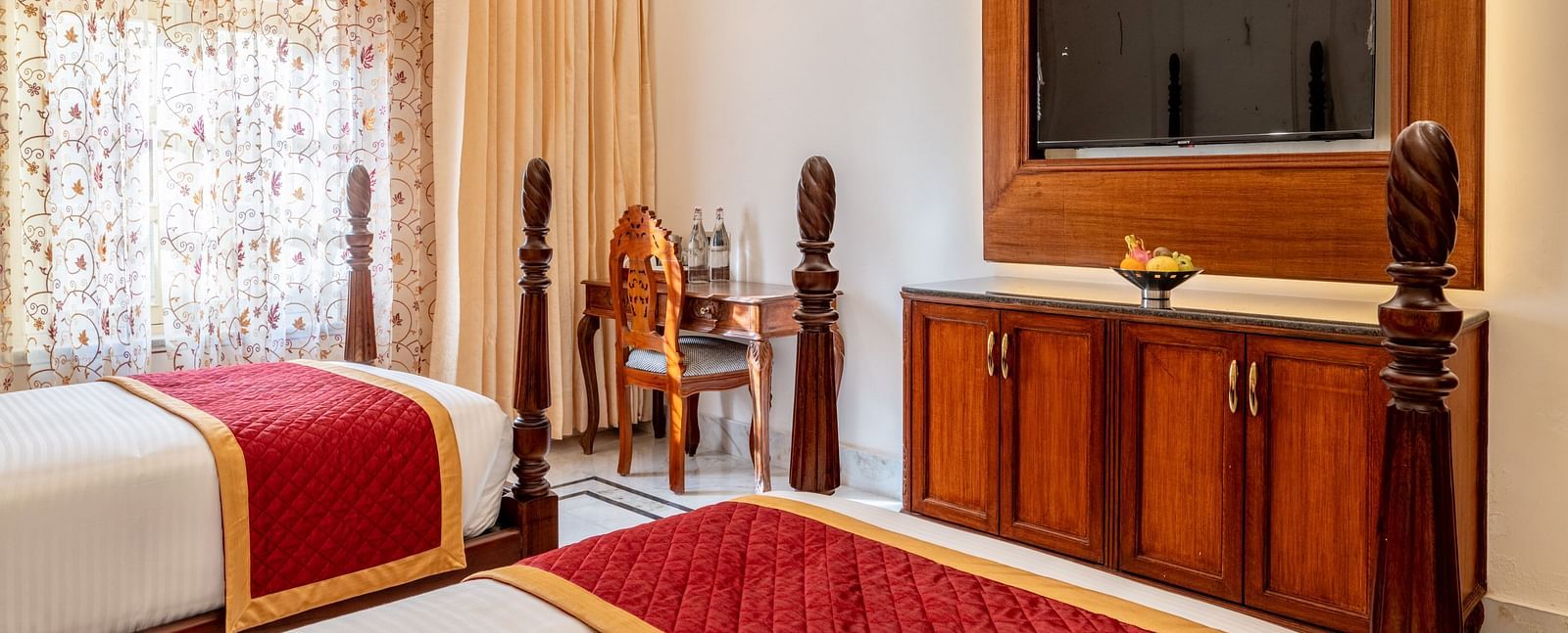 a room featuring a wall mounted television with a work desk and chair in the corner with natural light coming in from the window - Brij Castle, Jaipur