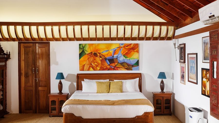 A room with wooden interiors featuring a bed, bedside tables, and paintings hung on the wall - BluSalzz Villas - Muhamma Resort, Alleppey