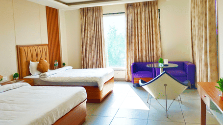 Executive Room at The Prince ZENQ Xpress Resortt Rohtak with two twin beds featuring wooden bases, a bright window with light brown curtains, a purple sofa, and a white chair.