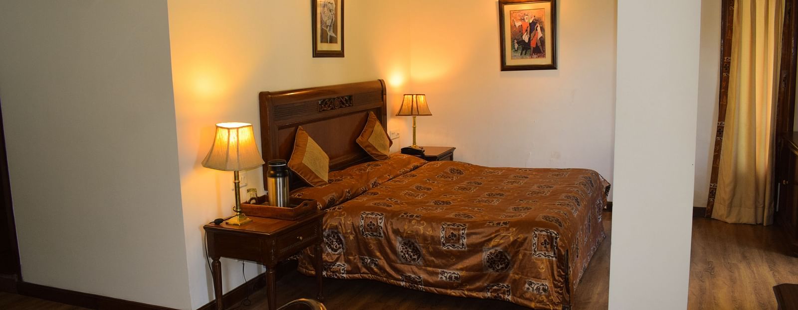 A wide view of a bedroom with a double bed with side lamps on both sides of the bed and a work desk and chair on the other side of the room - Sun N Snow Inn, Kausani
