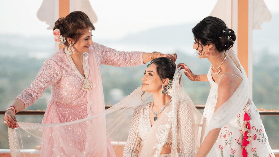 Two girls stand on either side of the bride, adjusting her dupatta at Fateh Vilas Collection Udaipur