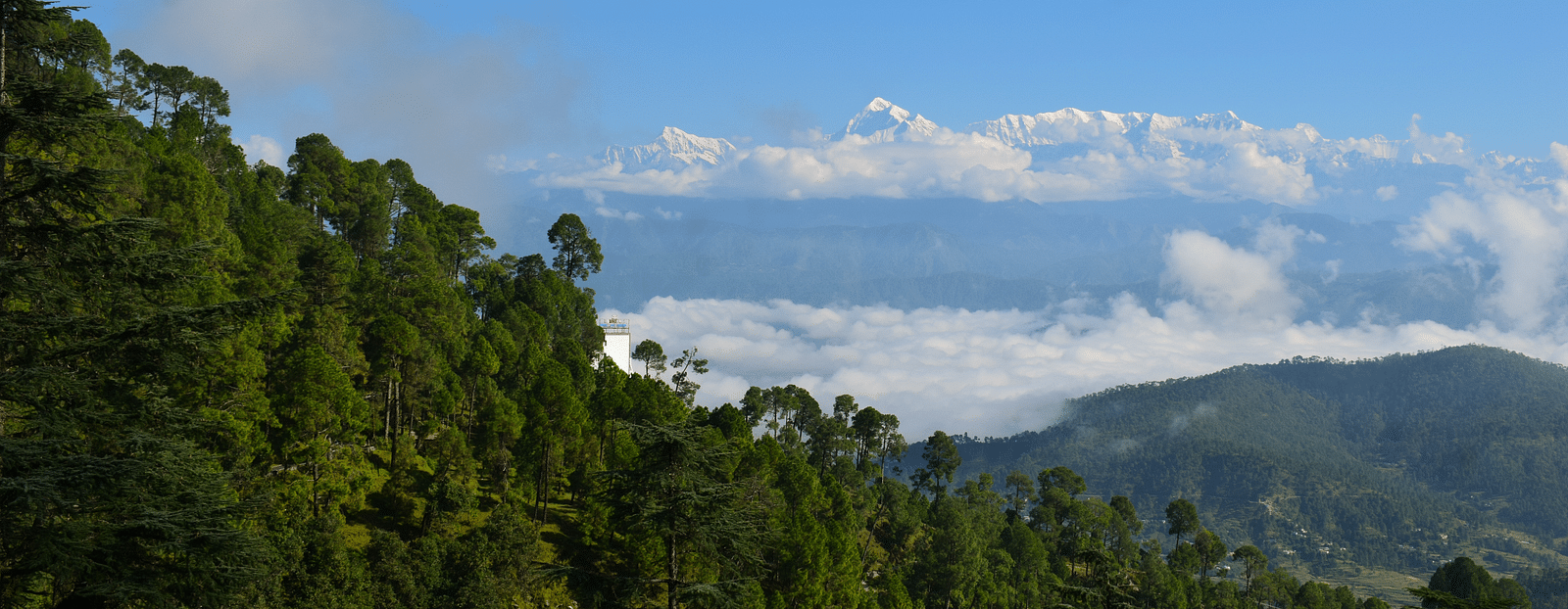 Panoramic view of lush green mountains with a winding road leading to a distant village.