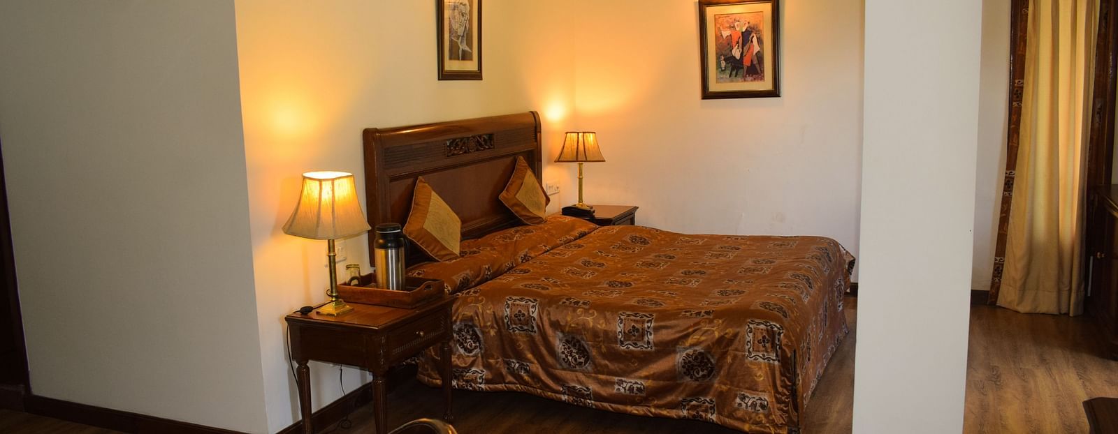 A wide view of a bedroom with a double bed with side lamps on both sides of the bed and a work desk and chair on the other side of the room - Sun N Snow Inn, Kausani