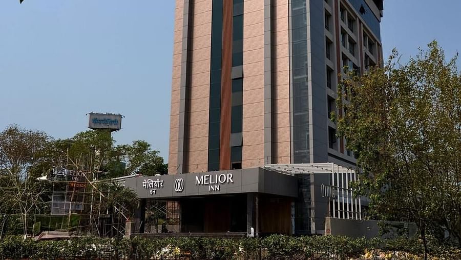 A multi-storey building with signage is visible against a bright sky with trees in the foreground - Melior Inn