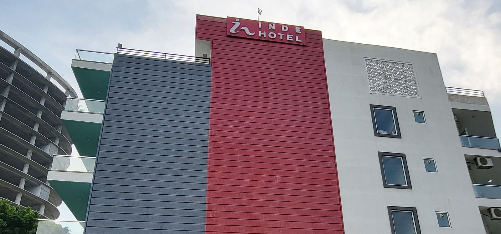 A facade image of Inde Hotel Golf Course extension featuring multiple storeys, balconies on each floor and a lawn in front of the property