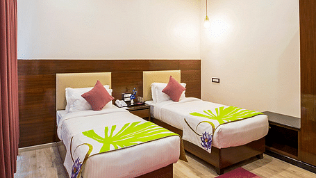 Corner view shot of the Deluxe Twin Room at Regenta Inn DLS featuring two single beds along with a bright red carpet on the floor.