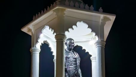 A tall white monument illuminated at night, showcasing an elegant statue beneath its glowing canopy.