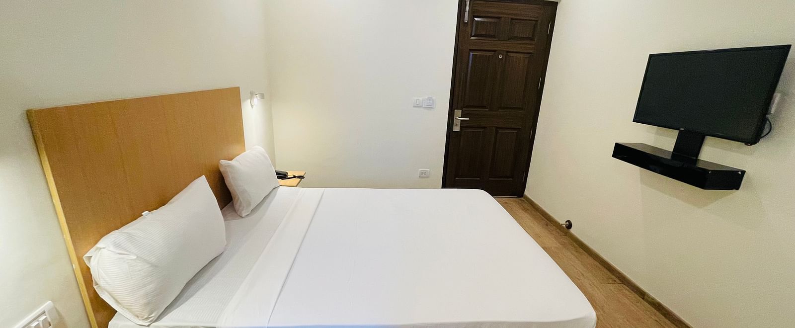 A double bed and a wall-mounted TV in a room at Sanctum Suites Richmond Road, Bangalore.