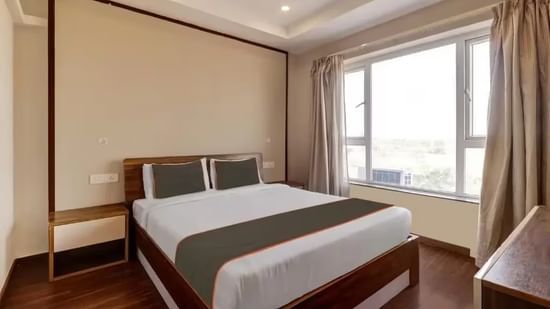 A hotel room with a double bed, dark headboard, and large window with light curtains - VITS Select Kailash Inn, Bagalkot