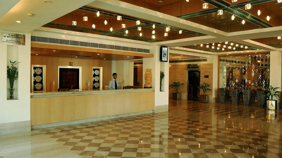 Spacious and well-lit hotel lobby with a check-in counter, receptionist, and polished marble floor with decorative lighting above in Lords Plaza Ankleshwar