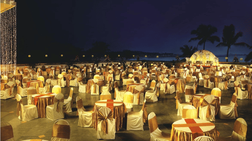 An outdoor evening event with round tables and chairs under string lights against a purple sky at The Retreat Hotel and Convention Centre.
