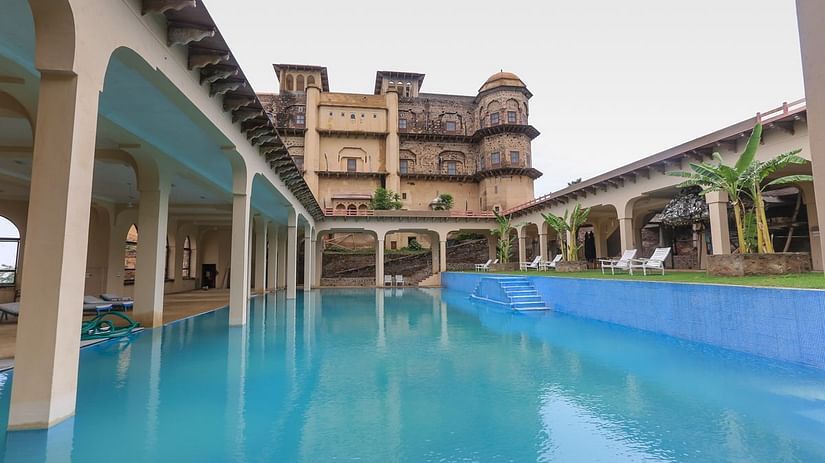 The swimming pool at Tijara Fort-Palace in Alwar, Rajasthan, reflects the historic architecture under an overcast sky.