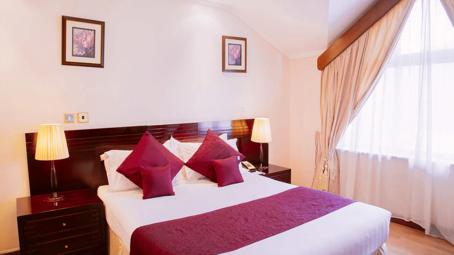 Standard Queen Room featuring a plush bed placed next to curtained window and wall hangings with lamps on both sides of the bed on nightstands at Boma Inn Nairobi