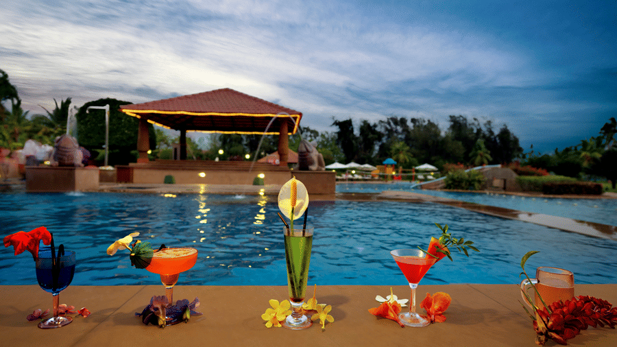 Bright coloured drinks are assembled in front of an exceptionally blue pool