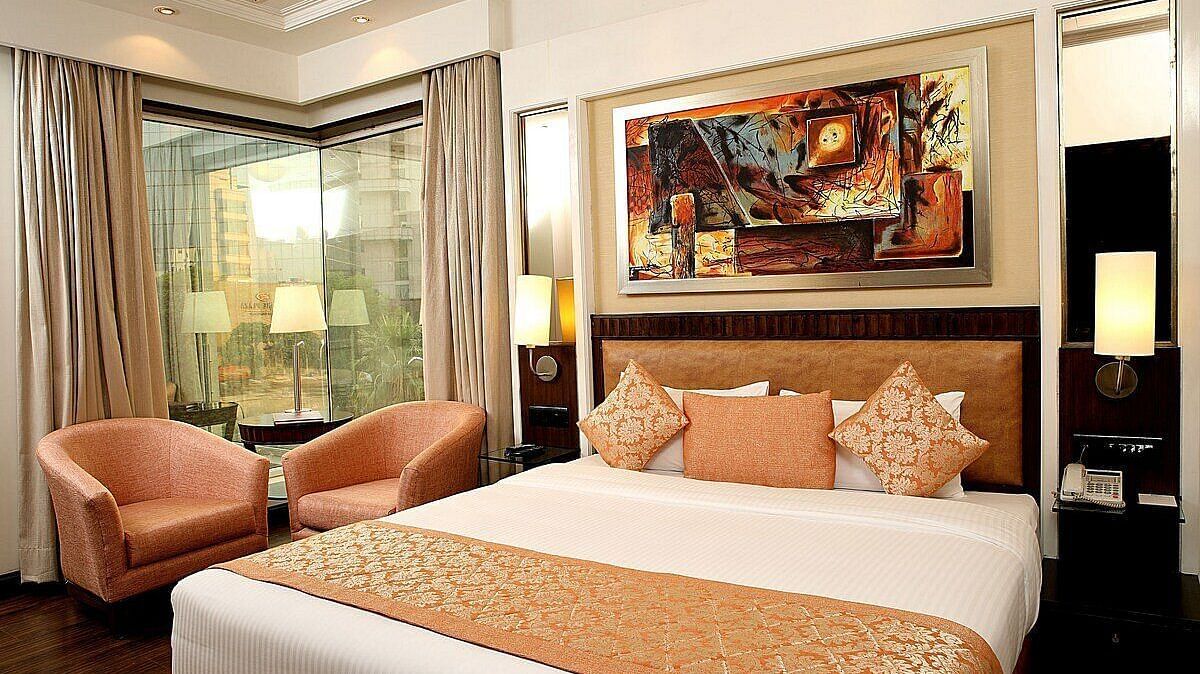 Executive Room with a double bed, bedside table with a lamp on top, cushioned seating with a table in front, and a window behind at Inde Signature Tower, Gurgaon