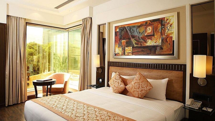 Executive Room with a double bed, bedside table with a lamp on top, cushioned seating with a table in front, and a window behind at Inde Signature Tower, Gurgaon