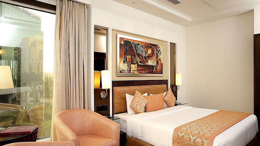 Executive Room with a double bed, bedside table with a lamp on top, cushioned seating with a table in front, and a window behind at Inde Signature Tower, Gurgaon