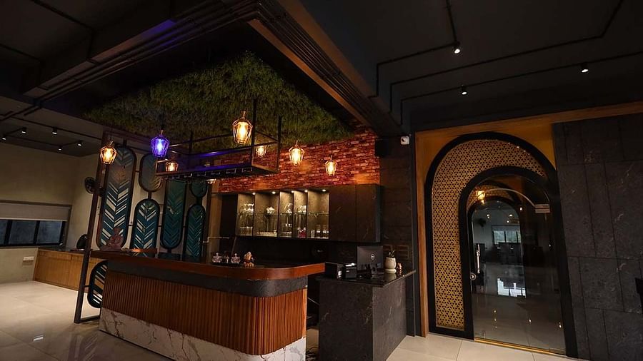 The image shows a bar area with stools, hanging lights, and decorative elements in a dimly lit setting - Lords Eco Inn Navsari.