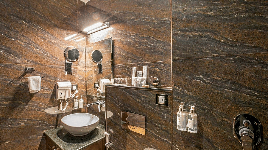A wide angle shot of the bathroom at Regenta Inn DLS showcasing a wash basin and a commode besides it.