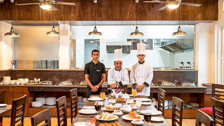 Three staff members of Regenta Inn DLS standing in front of a long dining table featuring a wide spread of delicious dishes.