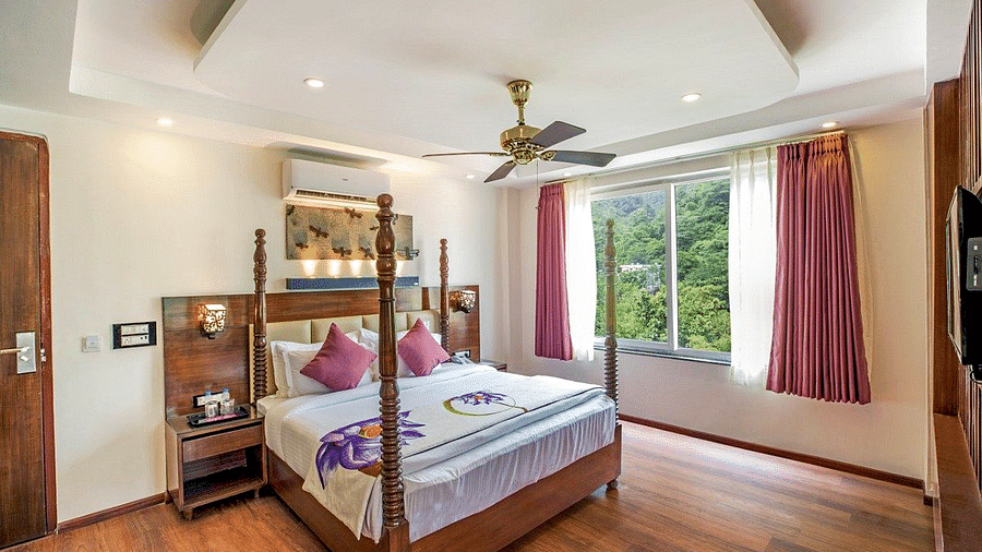 A comfortable double bed with a ceiling fan right above it on a false ceiling and a window besides it at Regenta Inn DLS.