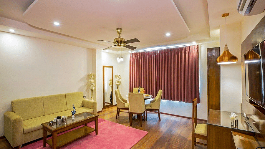 The living area of the Suite with the window covered with maroon curtains at Regenta Inn DLS.