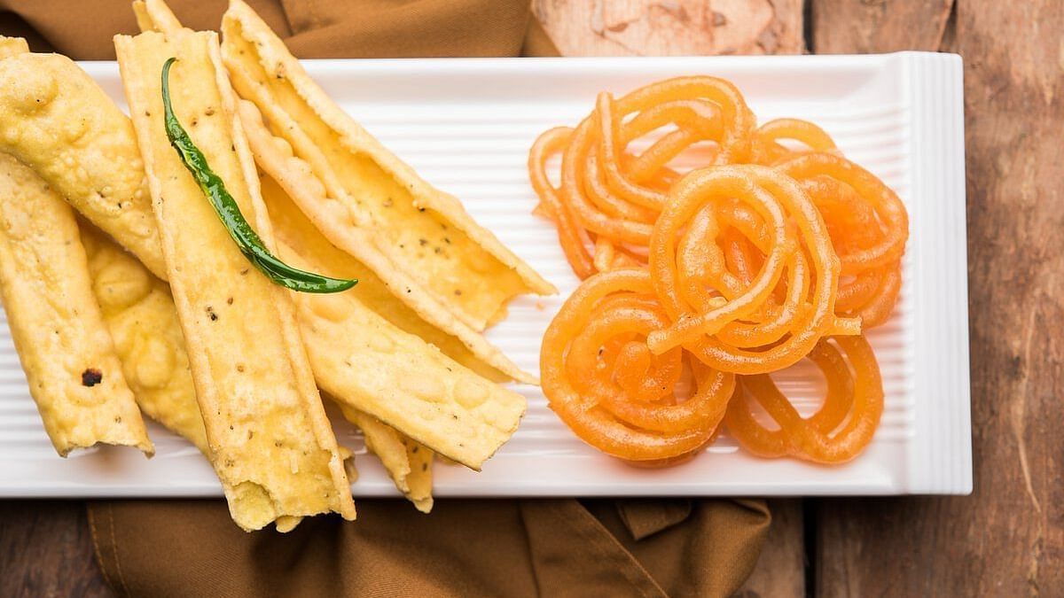 A rectangular white plate with crispy wafer snacks on the left garnished with a  chili, and bright  spiral-shaped sweets on the right. The plate is set on a wooden table.